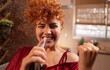 © Westend61 - Cheerful redhead woman imitating smart phone as microphone and holding fist at home