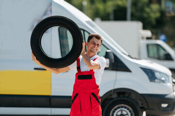 Young smiling man, in red coverall,  car mechanic holding auto tires