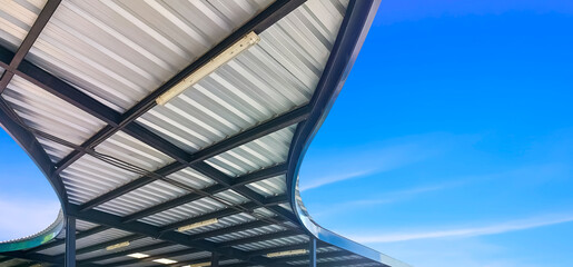 Wall Mural - Abstract curve pattern of corrugated steel roof with black metal roof beam structure of modern covered walkway against blue sky background, view from below and panoramic view