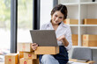 © David - Portrait business woman smile and use laptop checking information on parcel shipping box before send to customer. Entrepreneur small business working at home. SME business online marketing.