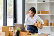 © David - SME concept. Young asian female ecommerce business owner prepares package box for customer and delivery check balance.  SME small business entrepreneur SME or freelance