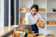 © David - SME concept. Young asian female ecommerce business owner prepares package box for customer and delivery check balance.  SME small business entrepreneur SME or freelance