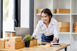 © David - SME concept. Young asian female ecommerce business owner prepares package box for customer and delivery check balance.  SME small business entrepreneur SME or freelance