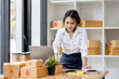 © David - SME concept. Young asian female ecommerce business owner prepares package box for customer and delivery check balance.  SME small business entrepreneur SME or freelance