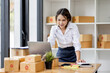 © David - SME concept. Young asian female ecommerce business owner prepares package box for customer and delivery check balance.  SME small business entrepreneur SME or freelance