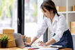 © David - SME concept. Young asian female ecommerce business owner prepares package box for customer and delivery check balance.  SME small business entrepreneur SME or freelance