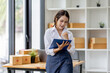 © David - Startup small business entrepreneur SME, asian woman checks stock on clipboard and parcels at home ,Success small business owner online sell marketing delivery, SME e-commerce telemarketing concept