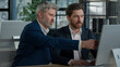 © Yuliia - Mature businessman mentoring man discussing project on computer consulting investor client about digital investment in office Caucasian businessmen colleagues working together discuss data management