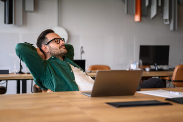 Wall Mural - tired young businessman with hands behind head and eyes closed taking a break at his desk in office