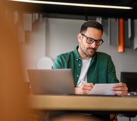 Wall Mural - focused financial advisor in glasses examining business report at desk while working in modern offic