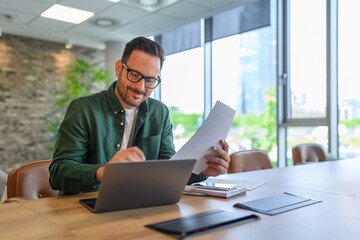 Wall Mural - handsome it engineer in eyeglasses smiling and developing online website over laptop on desk in offi