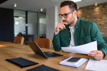 Wall Mural - focused young businessman auditing revenue report and planning budget while working at desk in offic