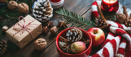 Sticker - An arrangement of Christmas items including a red bowl filled with pine cones a gift box in kraft paper pine branches a candle nuts anise apples and a red and white striped winter scarf on a dark woo