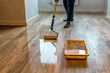 © Volodymyr Shevchuk - Worker varnishing floor with Eco white acrylic varnish for wood parquet floor, lacquering roller. Industrial theme. Home renovation