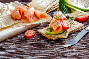 Poster - Crispbread and avocado and salmon sandwiches on paper on a kitchen table with a dark tablecloth. Copy space for food and drink and products. Delicious nutritious breakfast concept.