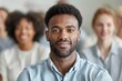 © Milos - A man sits among a crowd during a presentation or lecture, focused on the event with others also in attendance, all wearing formal or casual attire.