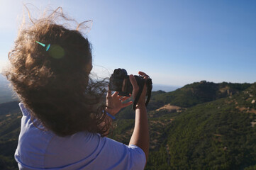 Woman with curly hair taking a photo of scenic mountain landscape on a sunny day