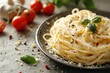 © Nena Photo - A mouthwatering serving of spaghetti topped with freshly grated cheese and herbs, set on a sleek black plate, complemented by garlic, tomatoes, and basil leaves.