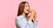 © Prostock-studio - Cheat meal day. Hungry young woman eating burger standing in studio on yellow background. Panorama
