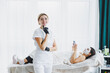 © DSMT - A cosmetologist wearing glasses and gloves performs a facial care procedure on a patient. A professional woman cosmetologist in a white coat with a well-lit office.