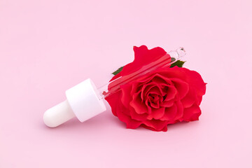 Wall Mural - Cosmetic serum pipette with face beauty serum inside on a pink background with red rose flower