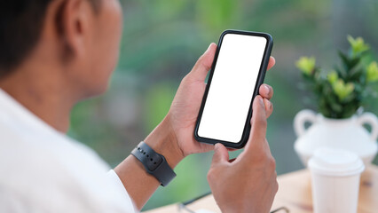 Wall Mural - Rear view of young man sitting at his workspace and using smartphone. Blank screen for graphics display montage.