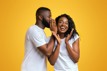 Wall Mural - African American Man Sharing Secret With His Woman, girl is surprised, yellow studio background