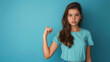 © BetterPhoto - A teenage girl in a blue shirt, standing against a matching blue background, making a fist with a determined expression, symbolizing strength and determination.