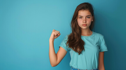 a teenage girl in a blue shirt, standing against a matching blue background, making a fist with a de