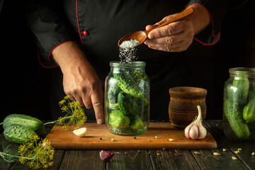 Wall Mural - Chef adding salt to a jar of cucumbers before canning. Concept of making delicious pickled cucumbers on the kitchen table by the hands of a cook