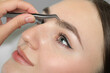 © New Africa - Beautician plucking young woman's eyebrow, closeup view