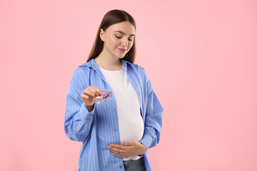 Wall Mural - Expecting twins. Pregnant woman holding two pacifiers on pink background, space for text