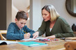 © CineLens2024/peopleimages.com - Mother, kid and homework with paper on table for learning, knowledge and support in education. Family, writing and woman with boy in house for child development, homeschool and help with studying
