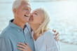 © peopleimages.com - Senior, couple and hug on beach with love on retirement vacation, romance and together with kiss for commitment. Man, woman and affection by ocean on summer holiday, happy and bonding with embrace.