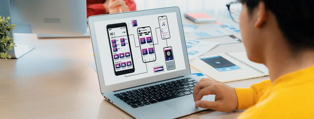 Panorama banner of startup UX developer or company employee design user interface or UI prototype for mobile application or website software with software display on laptop monitor in office. Synergic