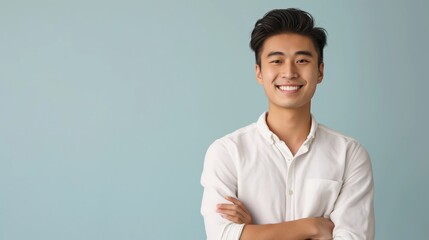 Wall Mural - Confident Young East Asian Man Standing with Arms Crossed, White Shirt, Light Blue Background