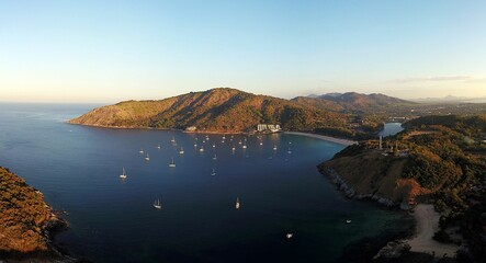 Sticker - Aerial view of a bay with yachts anchored, surrounded by lush hills and clear skies at sunset