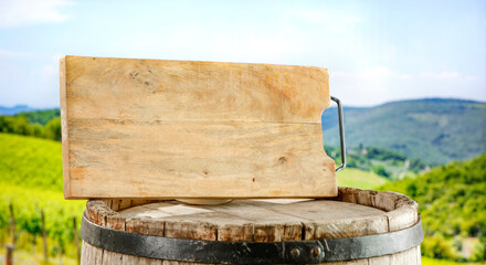 Canvas Print - Old wooden wine barrel with green grapevine leaf and blurred vineyard background. Copy space for products and food and drink.