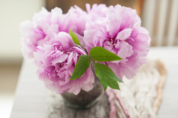 Beautiful freshly cut pink peonies in a vintage copper vase on old wooden board and linen runner in the background in front of a sunlit window