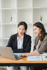 Wall Mural - Diverse beautiful Asian girls working together in modern office Collaborate at a table with a laptop and participate in discussions