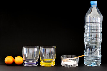 Eggs floating in saltwater experiment. First step in black background. Two eggs,  two glasses and a plastic bottle of water, a transparent ramekin full of salt with a wooden spoon on top. 