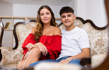 Wall Mural - Portrait of a smiling young married couple in an apartment, sitting on the sofa