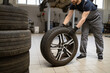© sofiko14 - Mechanic changing car tire in professional auto repair shop. Worker in uniform handling tire for maintenance and repair. Automotive service concept captured in garage environment.