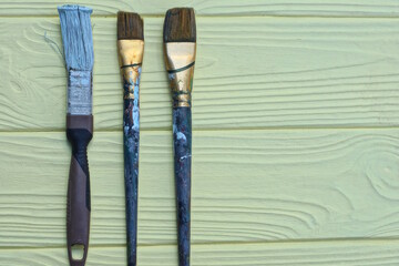 three dirty old paint brushes lie on a yellow wooden table