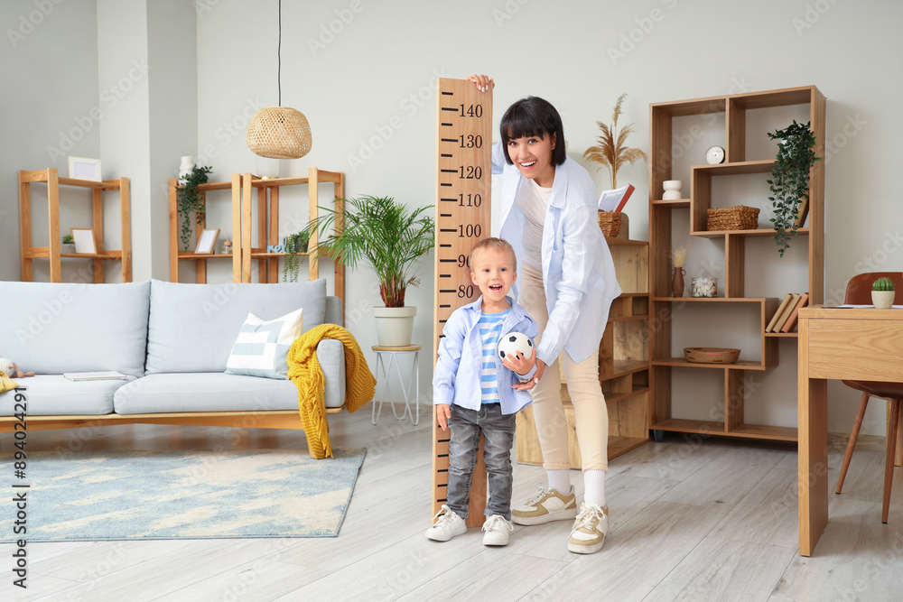 Young mother and her little son measuring height at home
