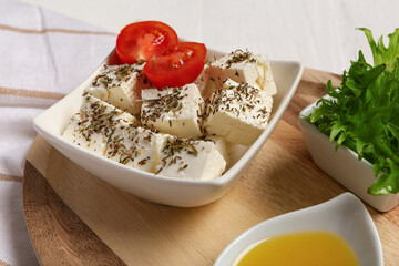 Canvas Print - Bowl with cubes of feta cheese, spices and cherry tomato on white wooden background