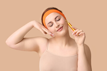 Sticker - Beautiful young woman using facial massage tool on beige background