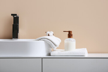 Wall Mural - Clean soft towels, bottle of cosmetic product and sink near brown wall in bathroom