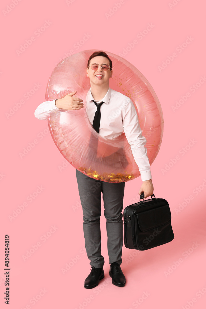 Office worker with inflatable ring and bag dreaming about vacation on pink background