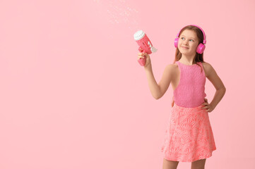 Poster - Happy girl in headphones with soap bubble gun on pink background